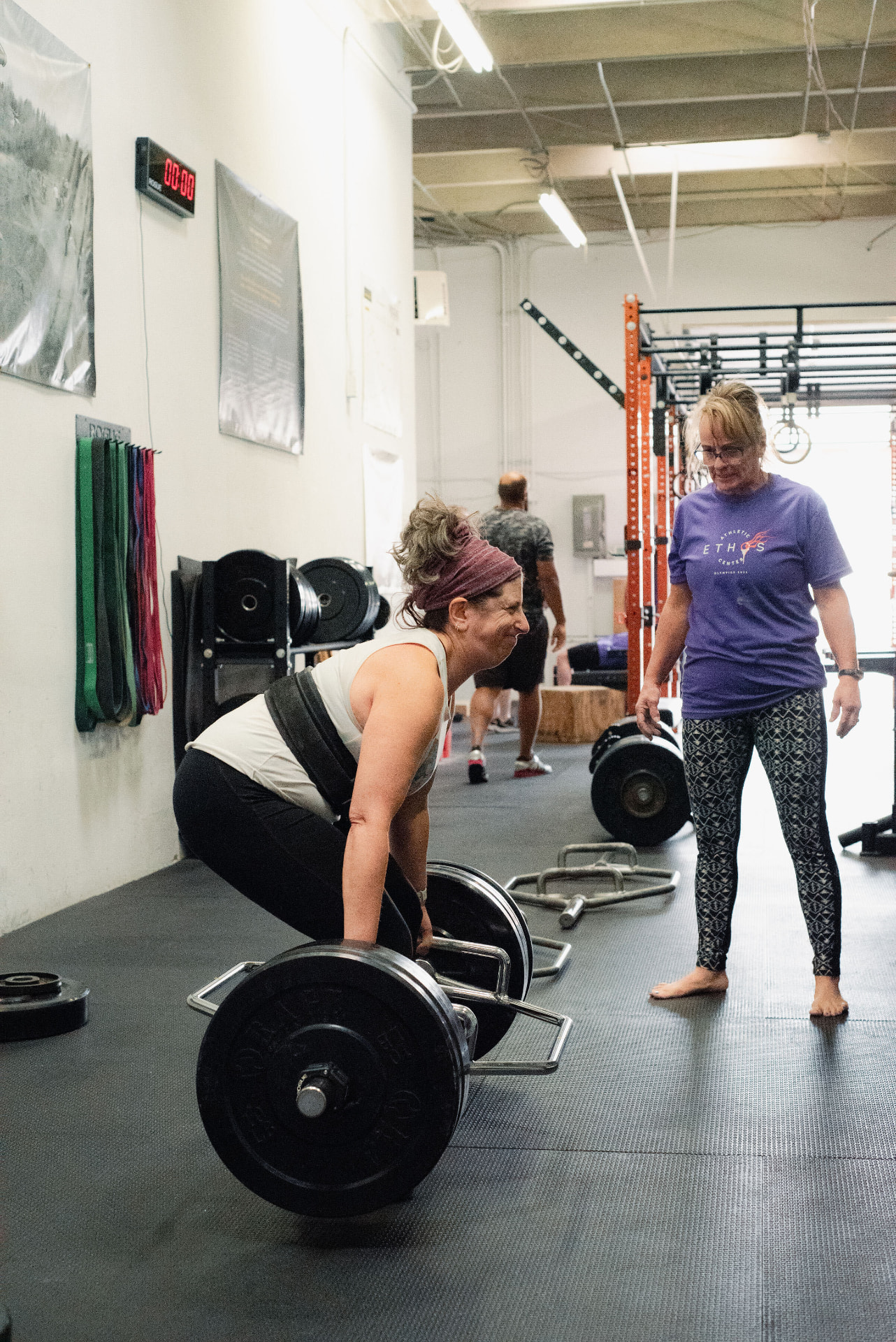 A woman setting up for a trap bar deadlift with a coach watching her form